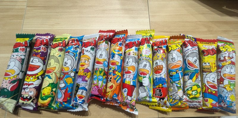 14 different Umaibo flavors lined up showing variety of Japanese dagashi corn puff snacks